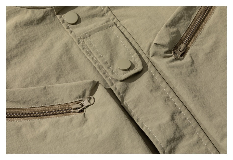 Close-up of a khaki jacket front with snap placket and two visible zippered pockets.