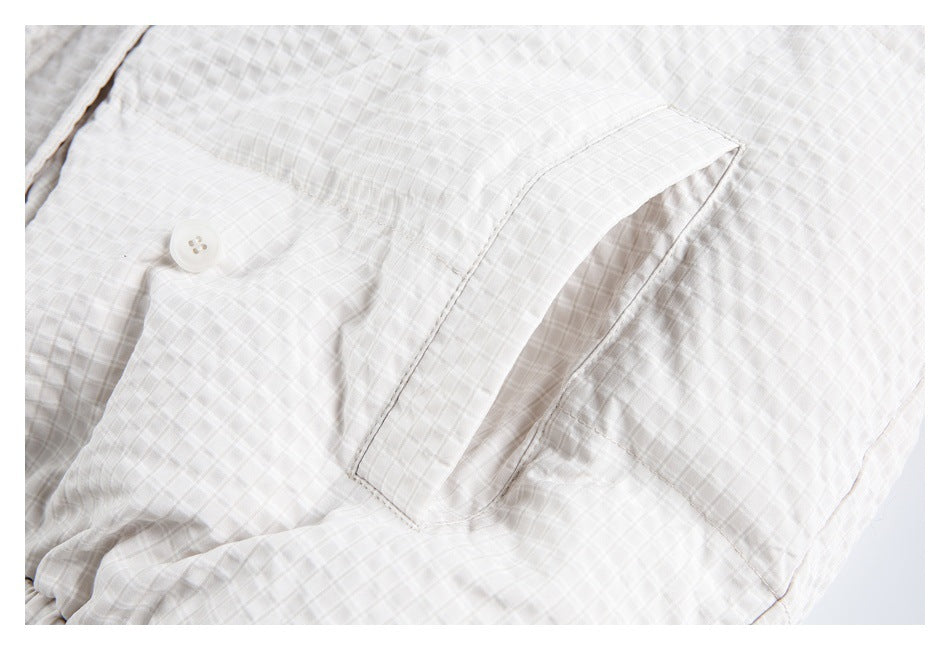 Close-up of a white and pale gray check garment with a buttoned flap pocket.