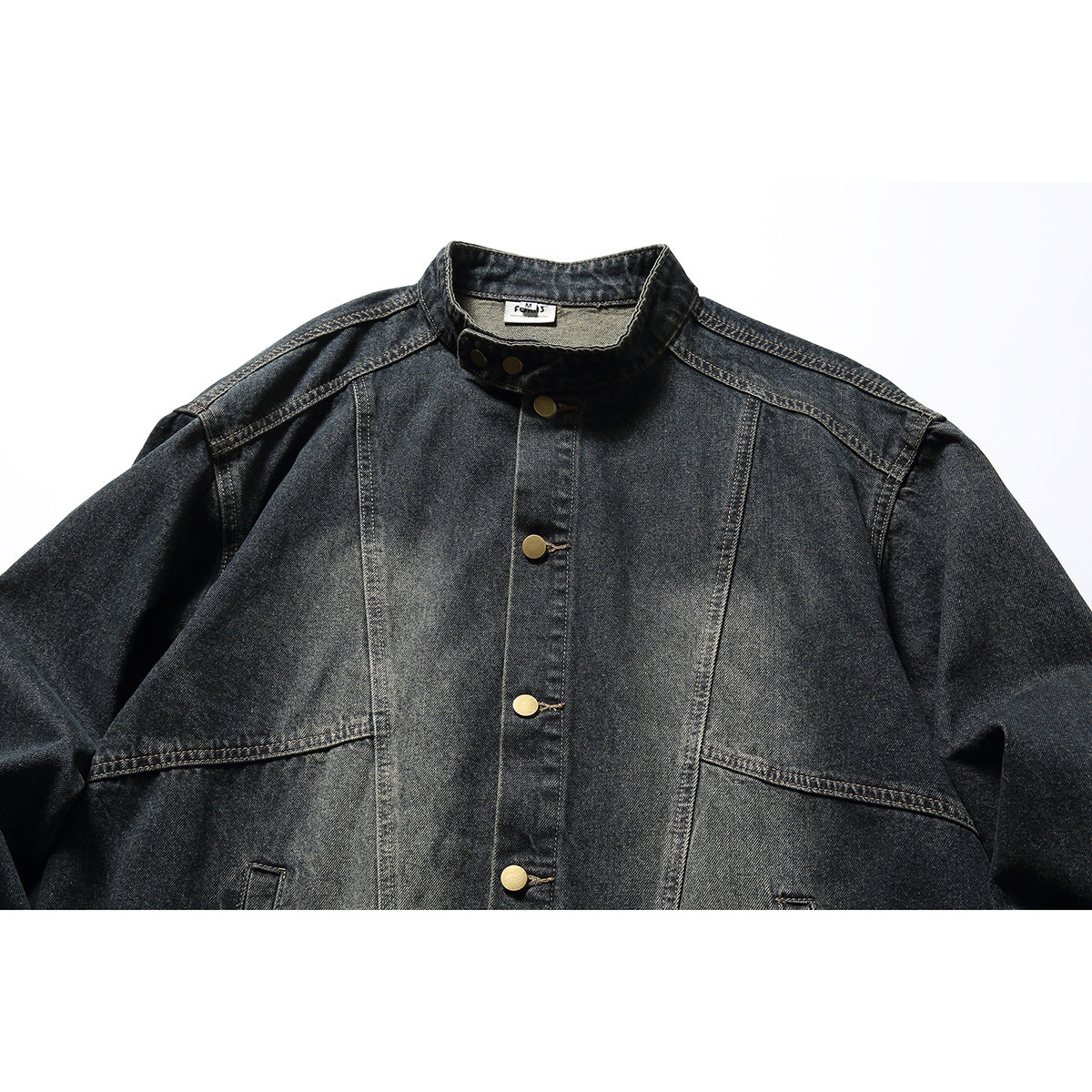 Close-up of the front of a black washed-denim jacket, showing its stand collar, brass buttons and seam panels.