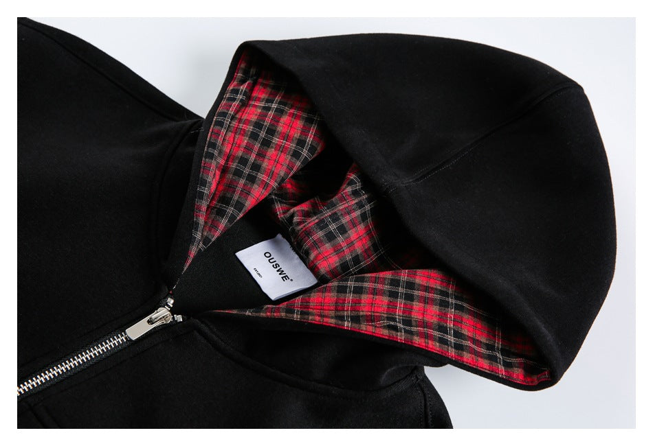 Close-up of a black zip hoodie showing its hood lined with red, black and white plaid fabric and a sewn label.