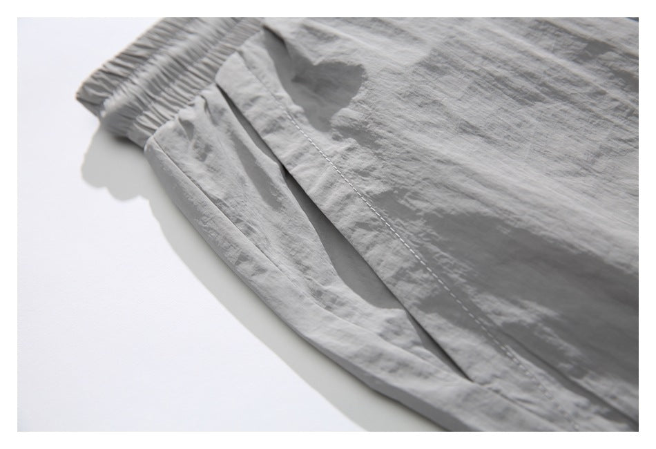 Close-up of light gray shorts showing the elastic waistband and stitched pocket opening.