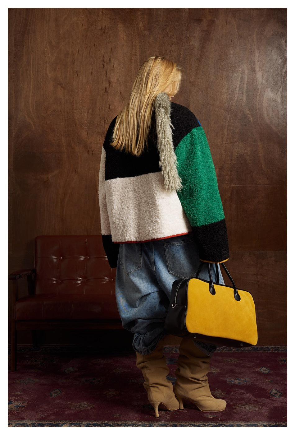 Back view of model wearing the color-block jacket with black, white, green and black panels, holding a yellow bag