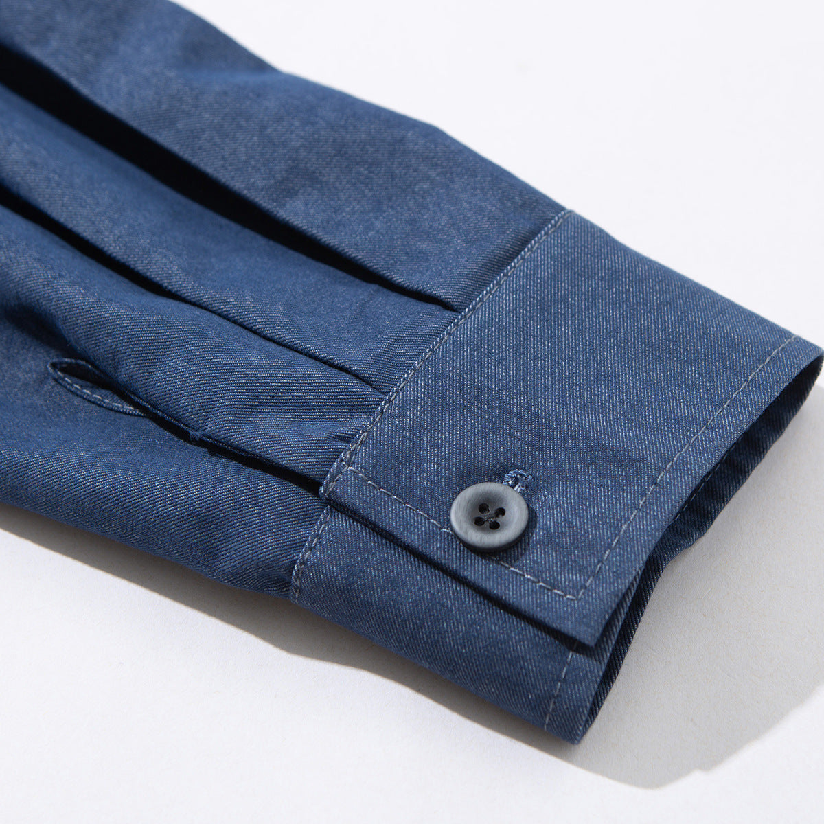 Close-up of a blue shirt sleeve cuff with a gray button and stitched buttonhole.