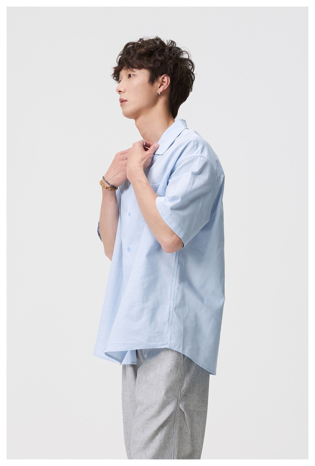 Side view of a man in a light blue short-sleeve camp collar shirt with gray pants, hands at collar