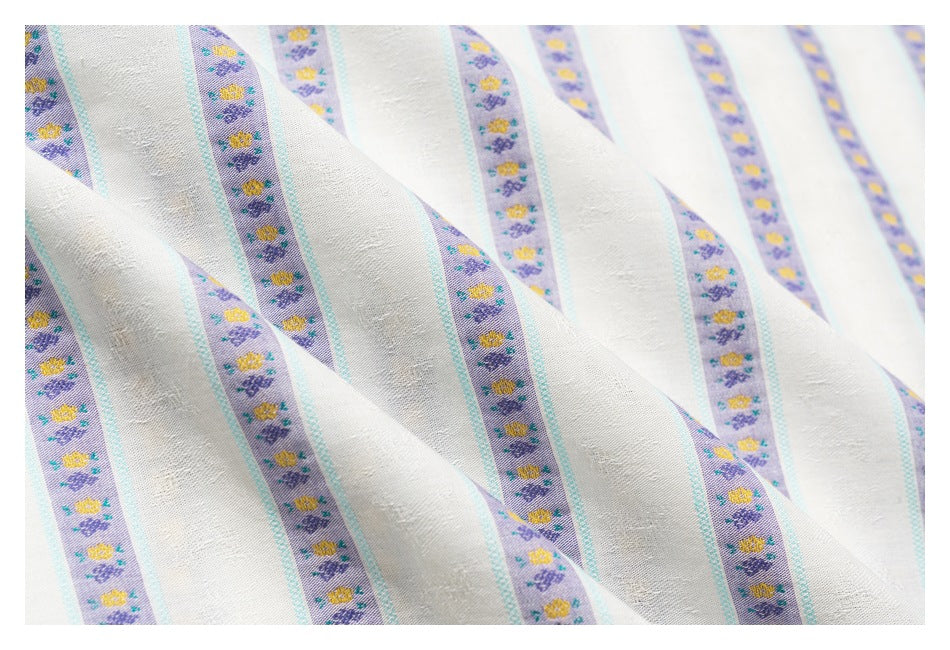 Close-up of ivory shirt fabric with lavender floral stripes and turquoise borders, draped to show its texture.