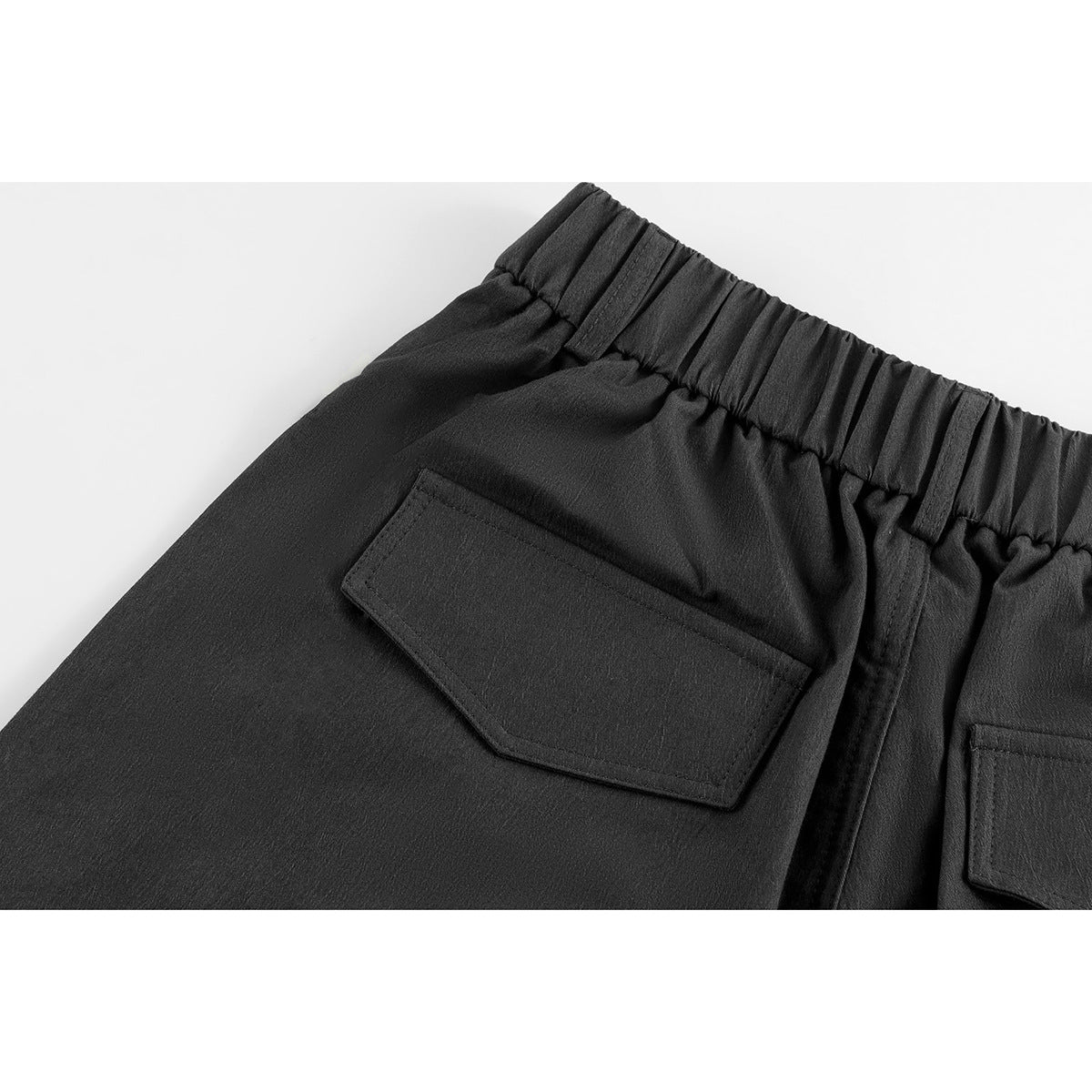 Close-up of black shorts from the back, showing an elastic waistband and flap pockets.