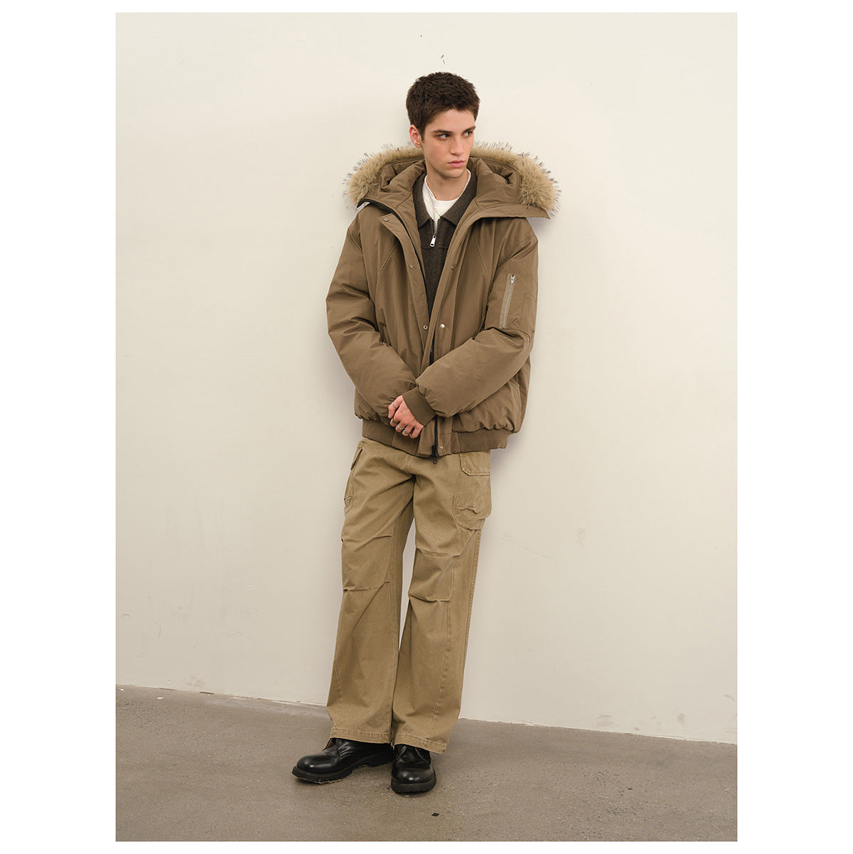Model wearing a taupe hooded parka with a fur-trimmed hood and khaki cargo pants.