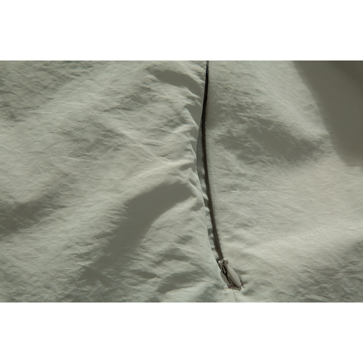 Close-up of the pale sage jacket's front zipper and lightly wrinkled fabric.