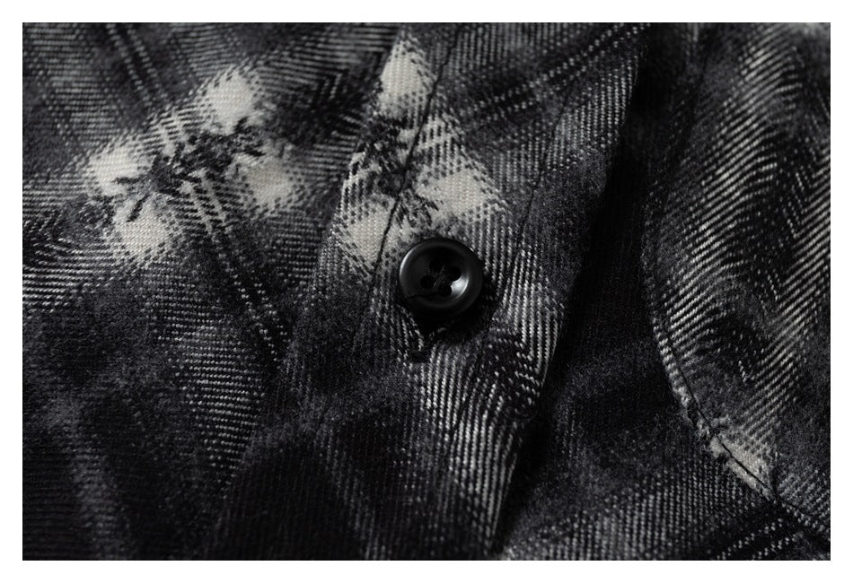 Macro view of a black button, stitching, and the shirt's black and gray plaid fabric.