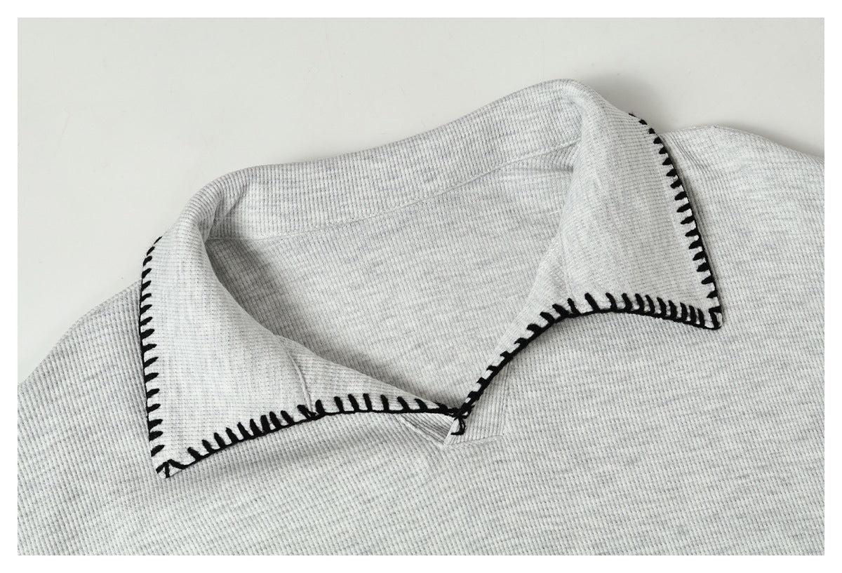 Close-up of a light gray ribbed garment collar edged with bold black blanket stitching.
