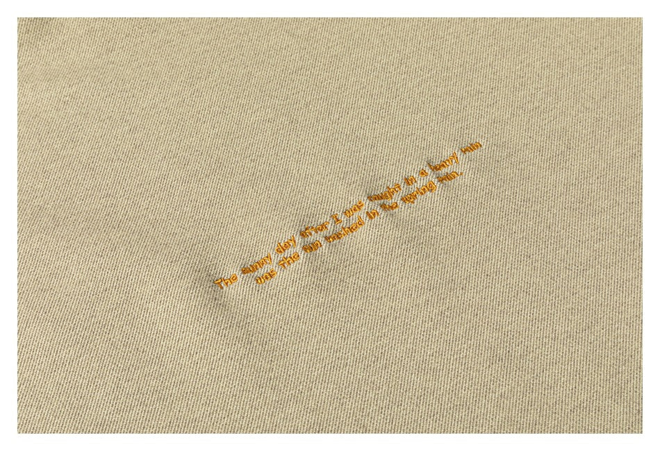 Light beige garment fabric with a small line of gold embroidered English text.