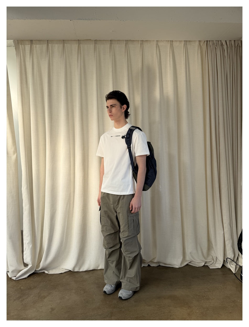 Model in white short-sleeve T-shirt with chest print, olive cargo pants and a navy backpack, angled side view