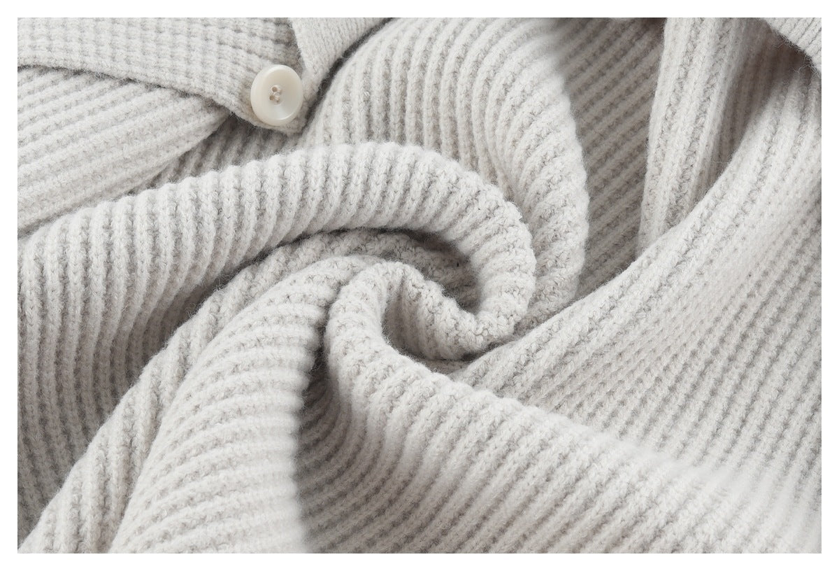 Close-up of a light gray rib-knit cardigan with a cream button and softly draped folds.