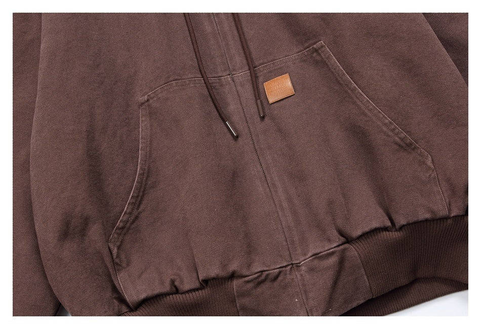 Close-up of the brown hoodie’s kangaroo pocket, drawstrings, small tan patch, and ribbed hem.