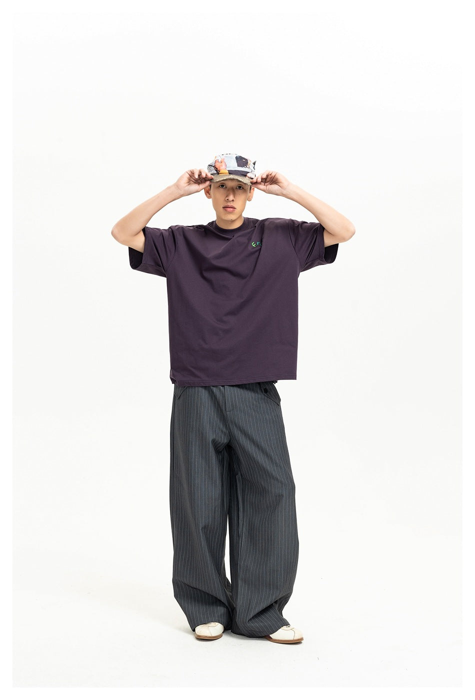 Full-length front view of a model wearing a dark plum oversized T-shirt with a small green chest graphic and pinstriped