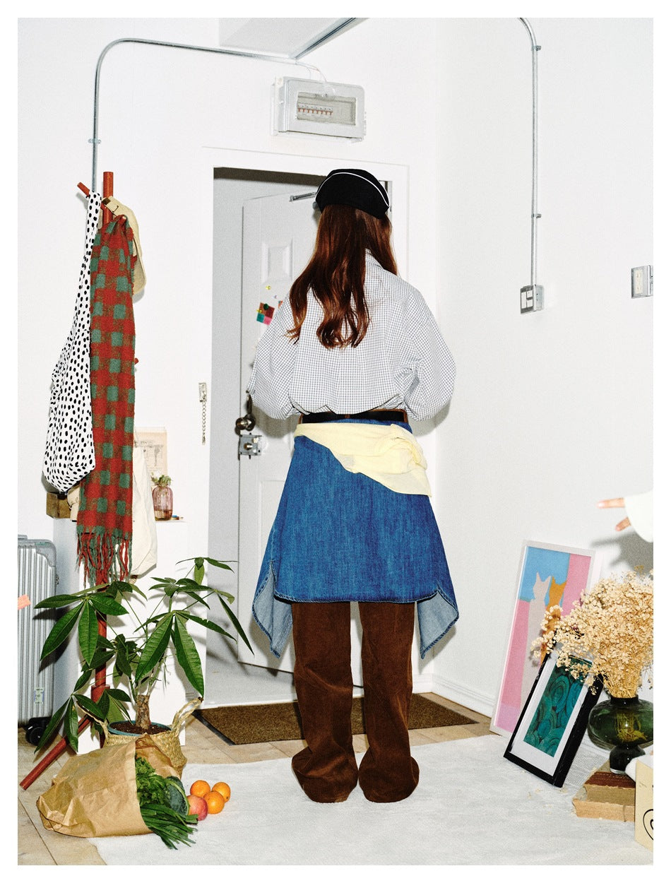 Back view of a model wearing a gray-and-white check shirt, brown trousers, and blue denim tied around the waist.