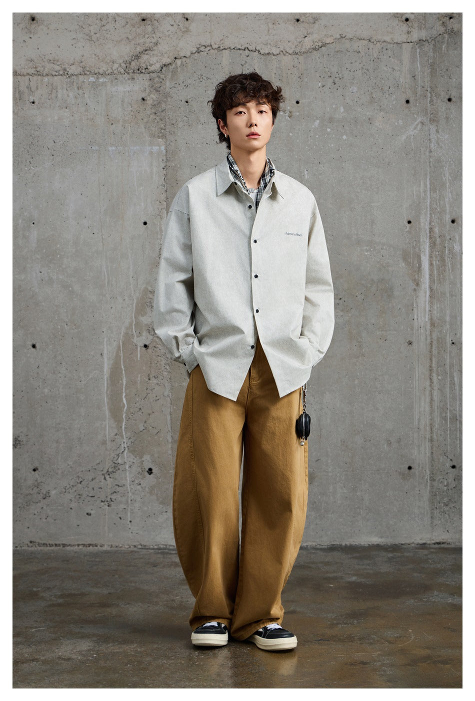 Full-length view of a model in a light gray oversized shirt, brown wide-leg trousers, and dark sneakers.