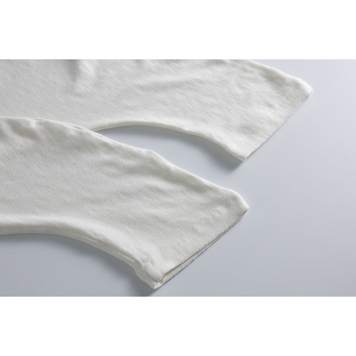 Close-up of two off-white T-shirt sleeve hems laid flat against a pale gray background.