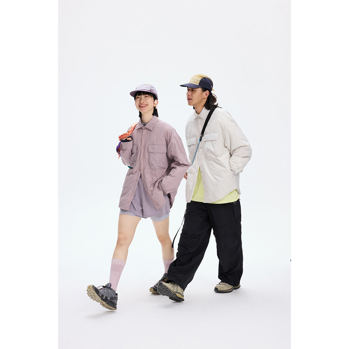 Two models wear oversized utility shirts: one in dusty mauve with shorts, the other in ivory with black pants.
