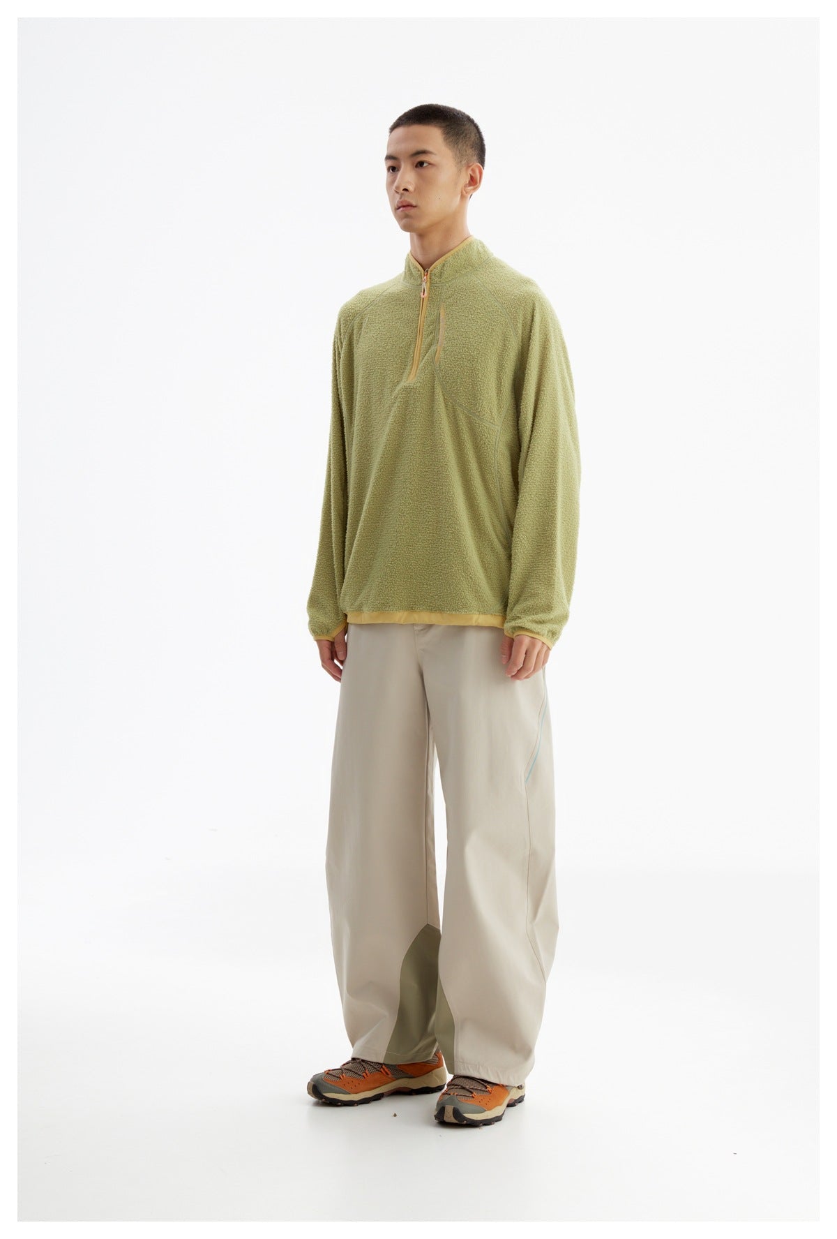 Full-length model wearing a light olive textured quarter-zip pullover with tan trim and loose beige trousers.
