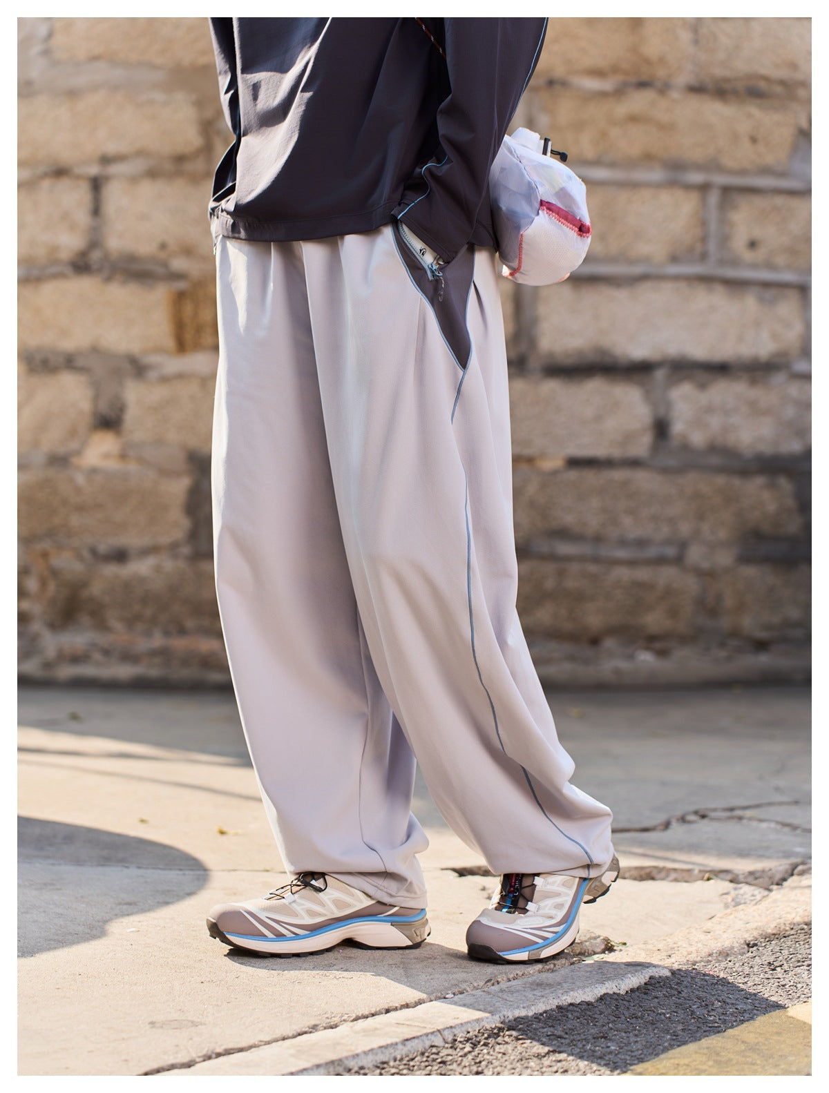 Side close-up of loose light-gray trousers, showing blue piping and a dark zippered side pocket.