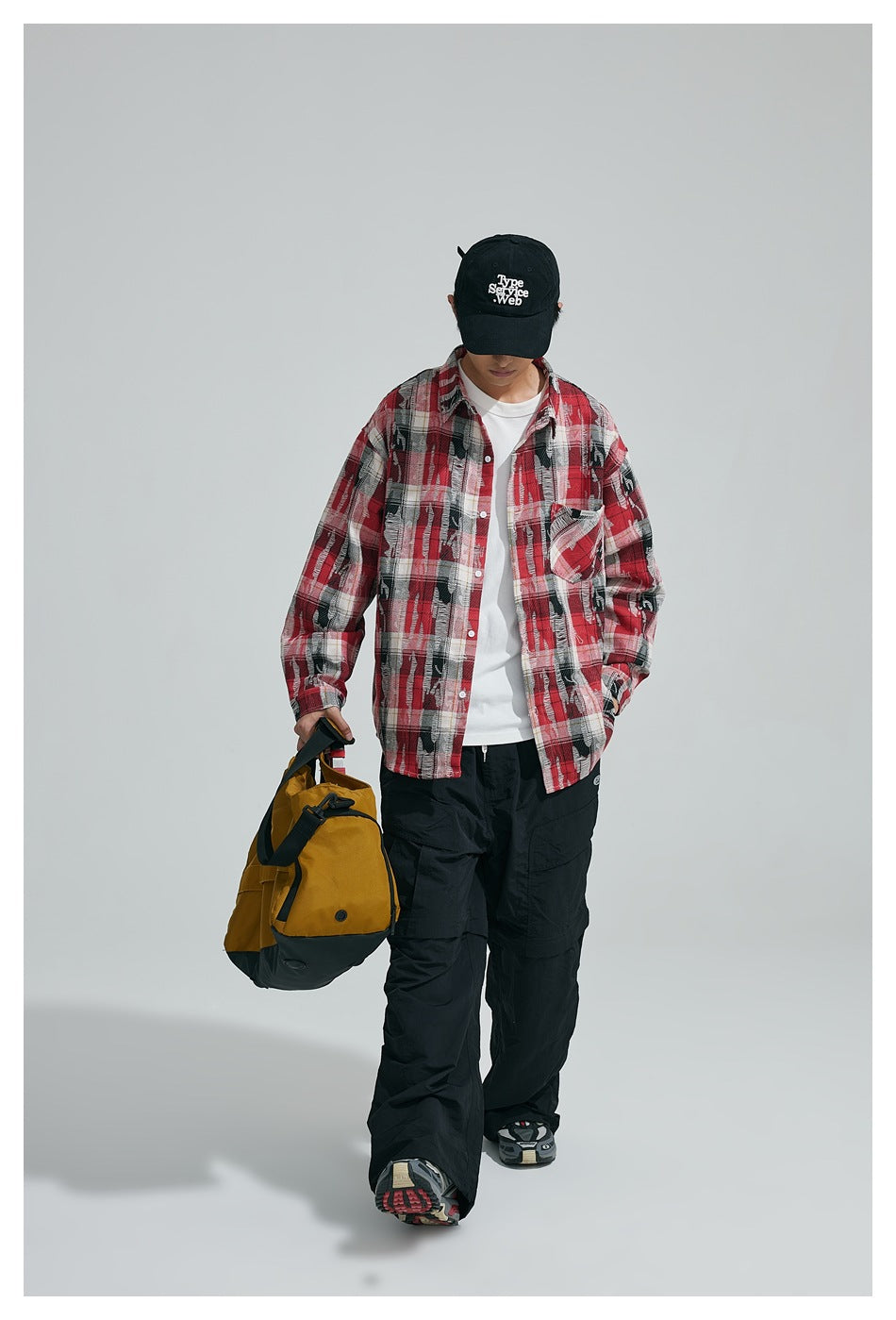 Model wearing an open red, black and white plaid shirt over a white tee, shown from the front.