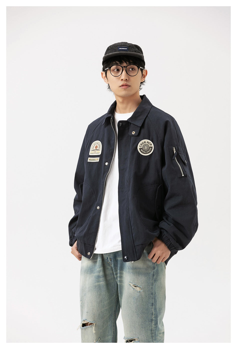 Model wearing navy bomber jacket partly unzipped, showing chest patches, sleeve zip pocket and ribbed hem