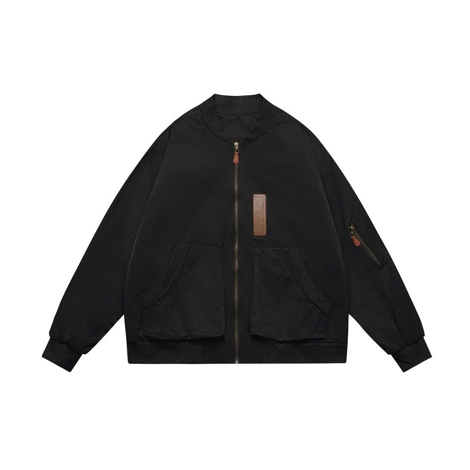 Black bomber-style zip jacket with ribbed collar, large patch pockets, sleeve zip pocket and brown chest tab, flat lay