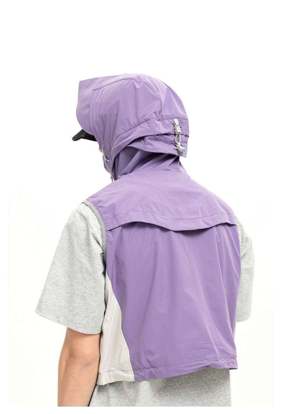 Close rear view of a model wearing a lavender hooded vest with pale side panels over a gray T-shirt.
