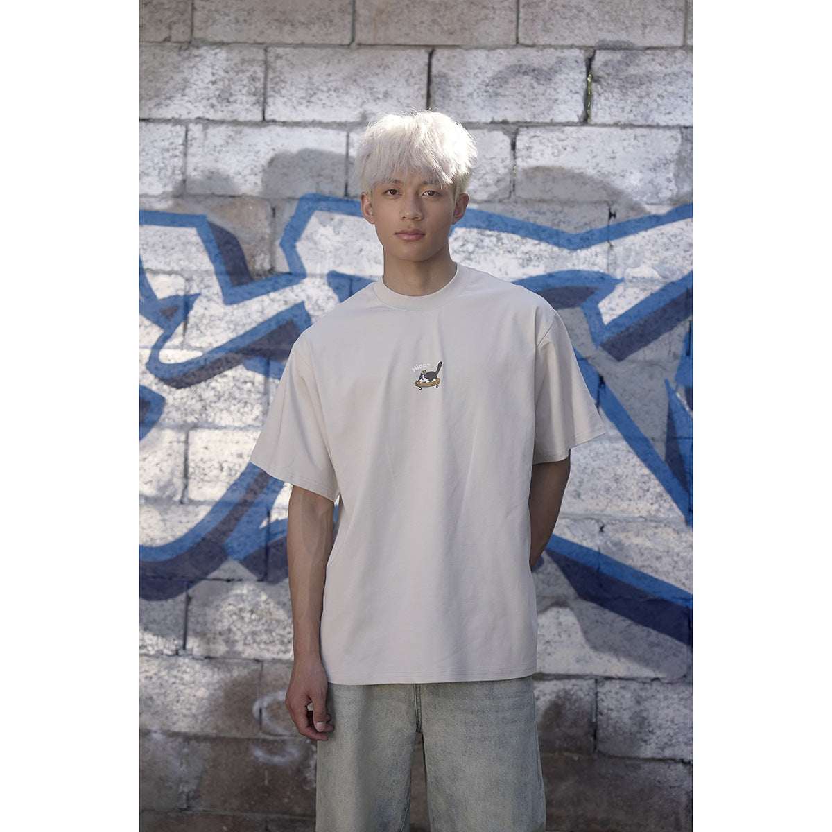 Model wearing an oversized light gray-beige crew-neck T-shirt with a small illustrated chest graphic.