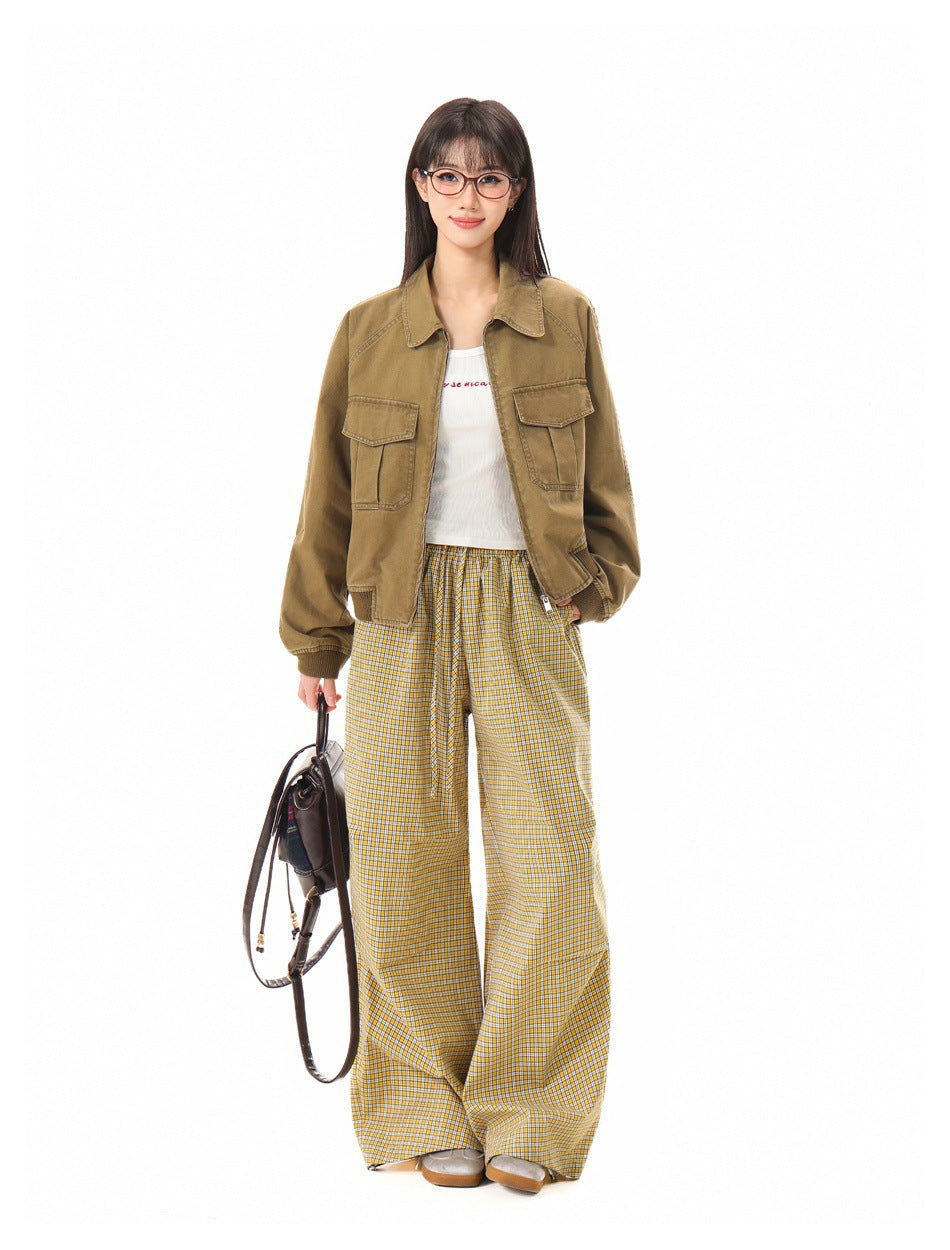 Full-length front view of a model in a tan utility jacket with flap pockets, yellow plaid wide-leg trousers, and a white top.