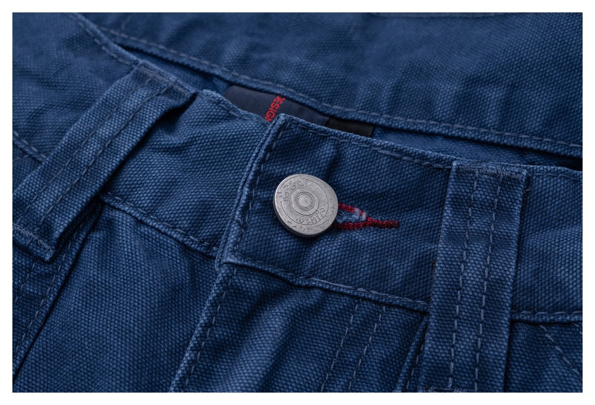 Close-up of dark blue trousers showing the waistband, belt loop, metal button and red stitching.