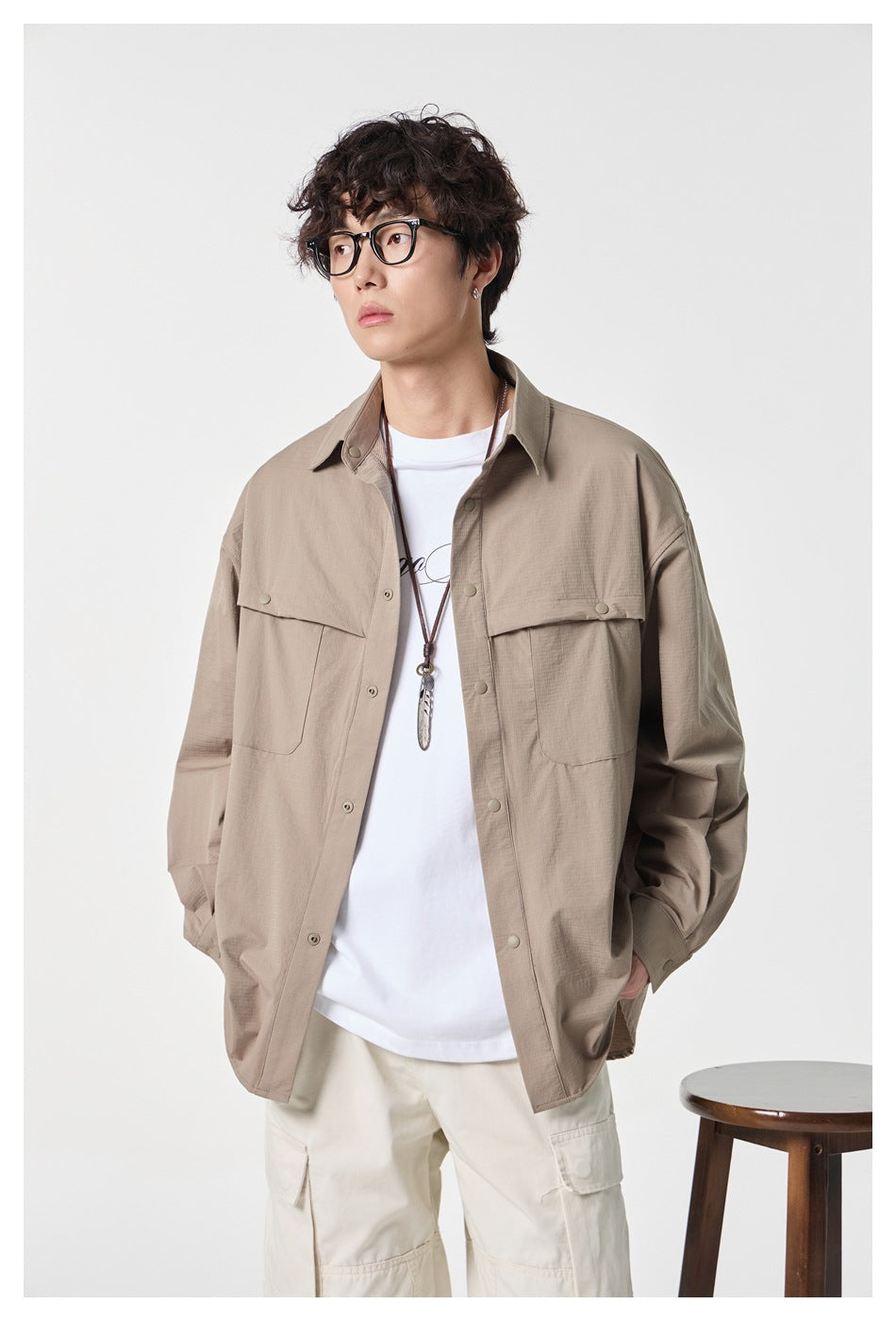 Front view of a model wearing an open taupe overshirt with two flap pockets over a white tee and cream cargo pants.