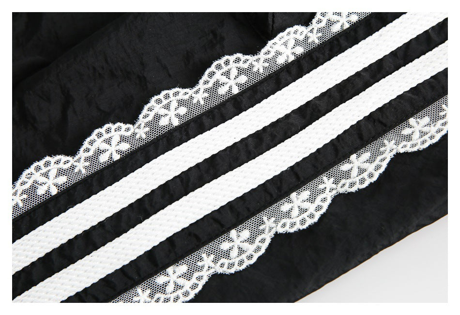 Close-up of black fabric with white floral lace trim and two wide white woven stripes.