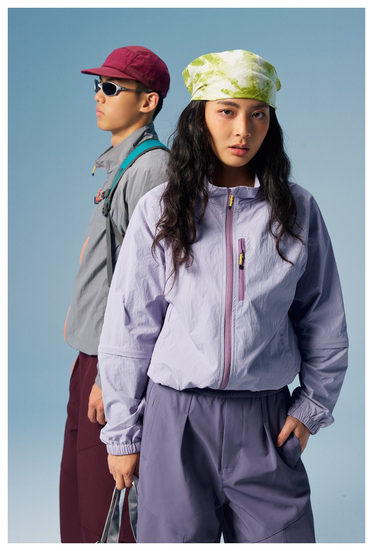 Close view of a woman wearing a lavender zip jacket and matching pants, with a man in gray behind her.