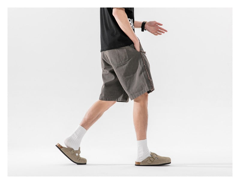 Rear side view of a model walking in charcoal shorts with a back pocket and frayed side seam.