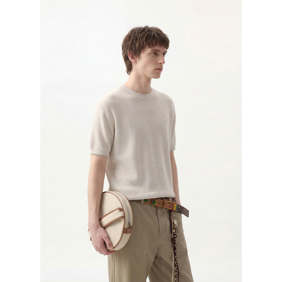 Model in an off-white ribbed short-sleeve crewneck top and khaki trousers, holding a cream shoulder bag; front three-quarter