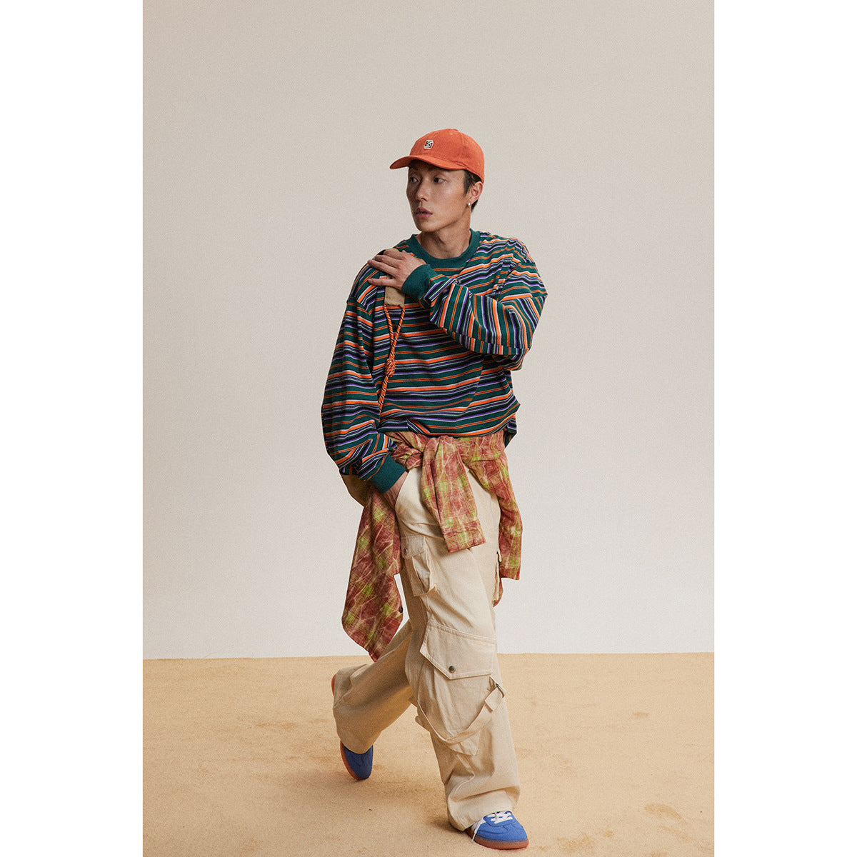 Model wearing a multicolored striped long-sleeve shirt, beige cargo pants and an orange cap.