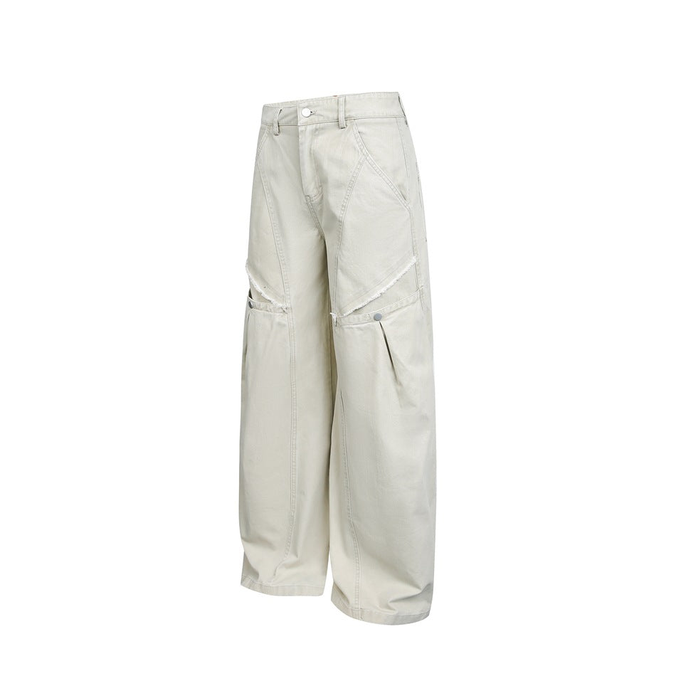 Light beige wide-leg pants displayed alone, with angled layered knee panels, button closures, and slanted pockets.