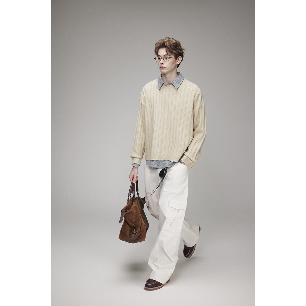 Model in a cream ribbed sweater layered over a checked shirt and paired with white cargo trousers.