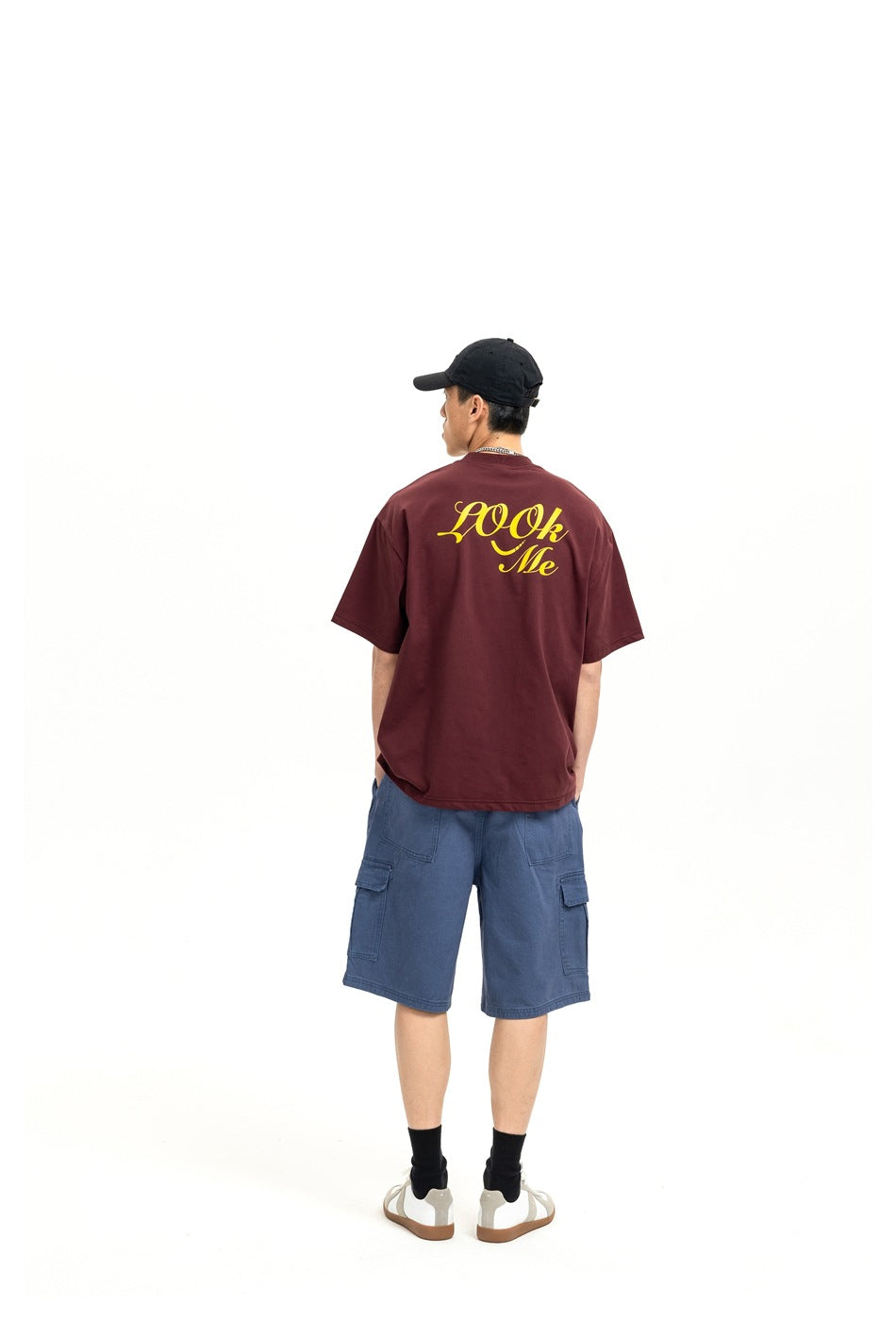 Rear view of a model wearing a burgundy short-sleeve T-shirt with yellow script on the back and blue cargo shorts.