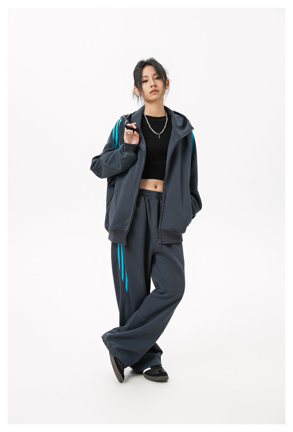 Model wearing dark gray wide-leg sweatpants with blue side stripes and a matching zip hooded jacket