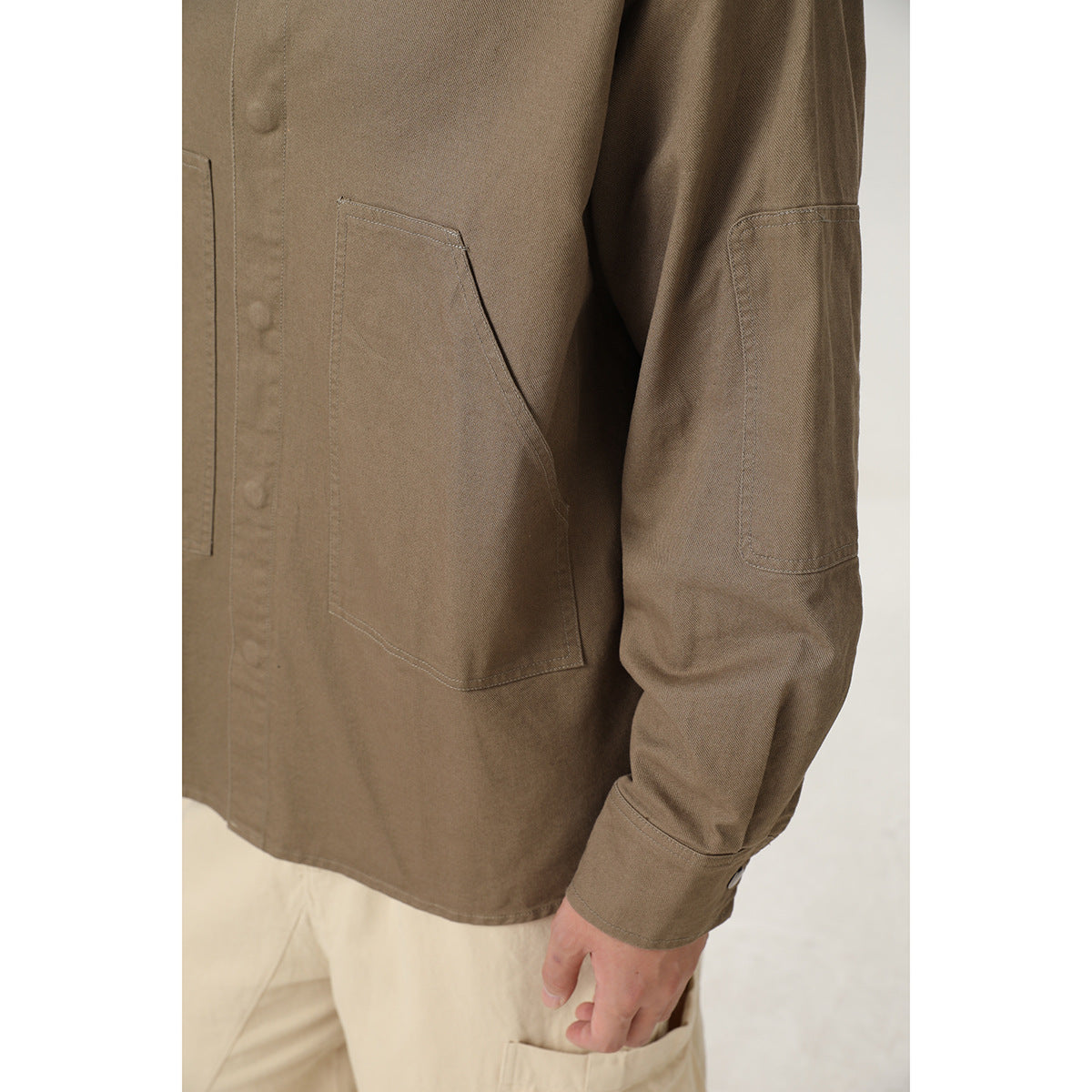 Close-up of the brown overshirt's large front pocket, sleeve patch pocket, stitching and button placket.