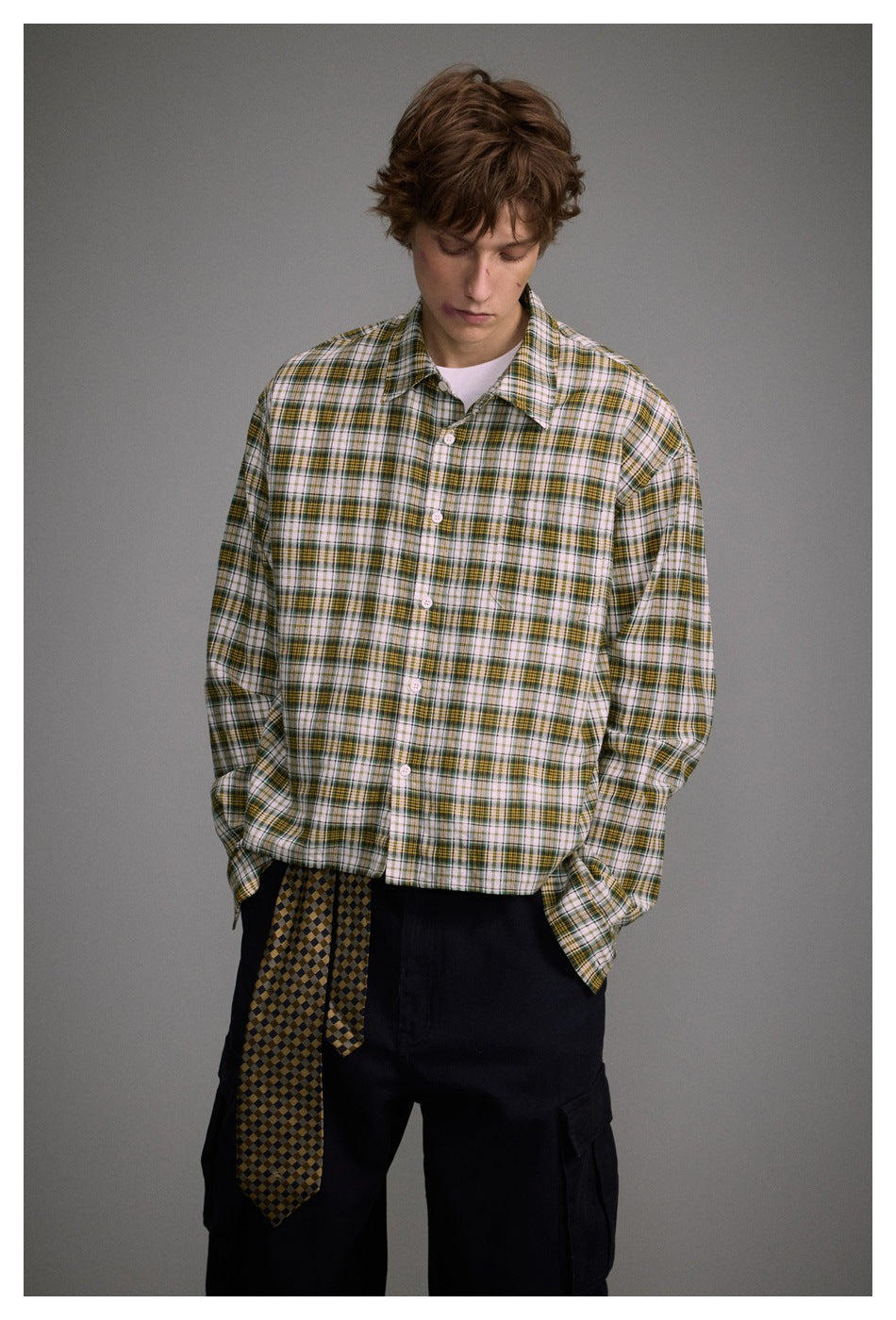 Model wearing a white, green, and mustard plaid shirt with black cargo pants and a patterned tie at the waist.