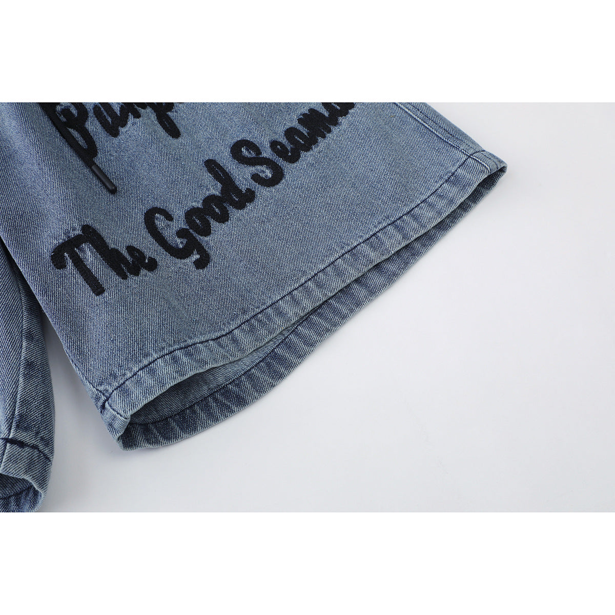 Close-up of the blue denim shorts' stitched hem and black script lettering.