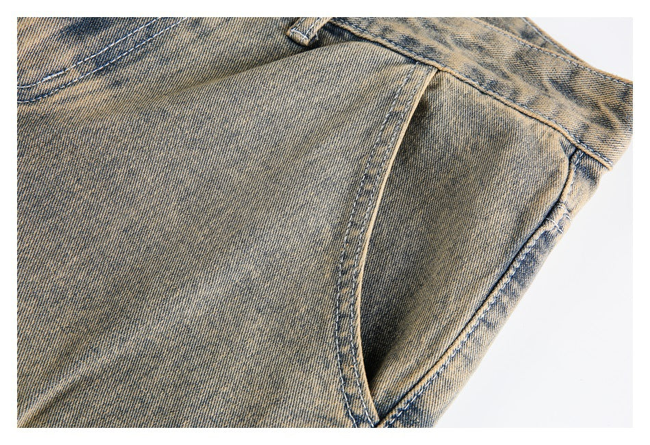 Close-up of a curved front pocket opening and stitched seams on tan acid-wash jeans.