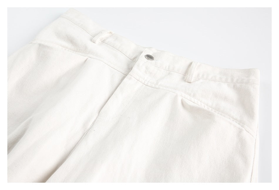 Close-up of ivory trousers laid flat, showing the waistband, button closure, belt loops, and front pleats.