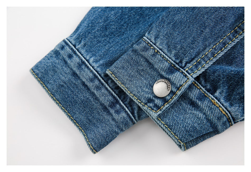 Close-up of a blue denim cuff tab fastened with a metal button and tan stitching.