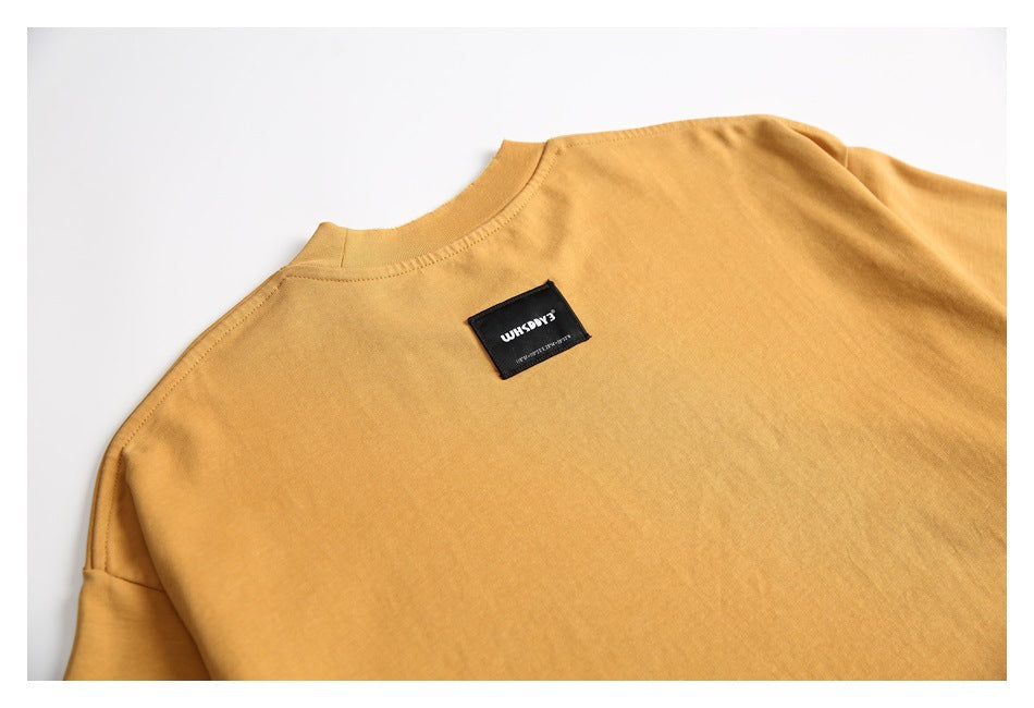 Angled close-up of the mustard T-shirt's upper back, crew neckline, and small black label.