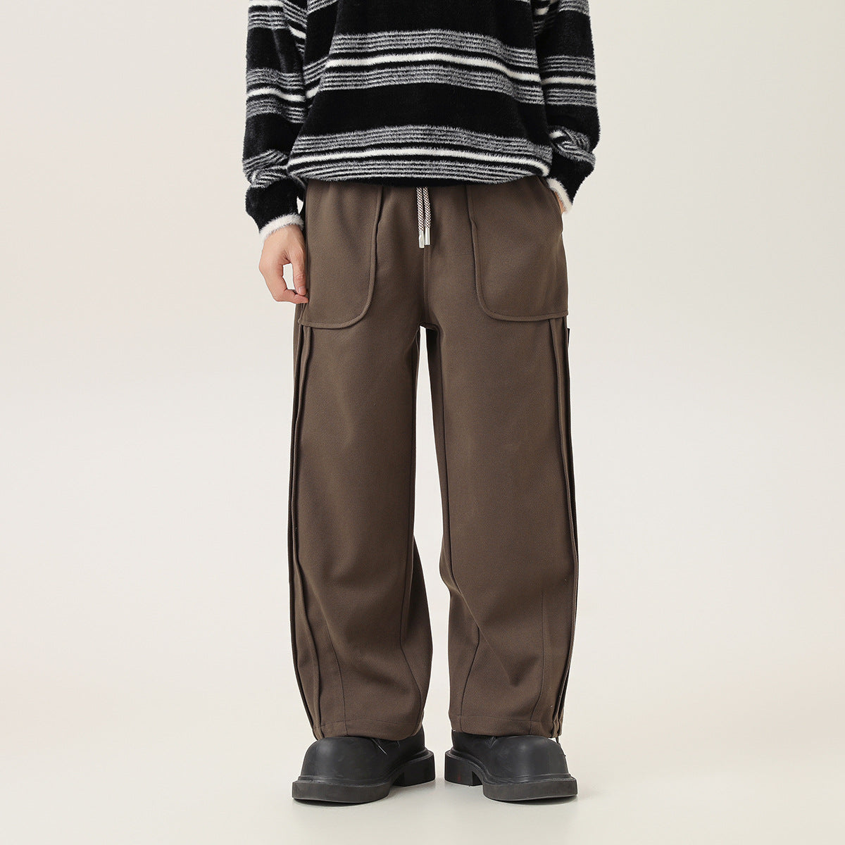 Front view of a model wearing loose brown drawstring pants with large front pockets and tapered cuffs.